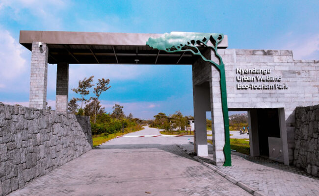 Entrance gate to Nyandungu Urban Wetland Eco-Tourism Park with stone walls and a green tree sculpture over the arch.